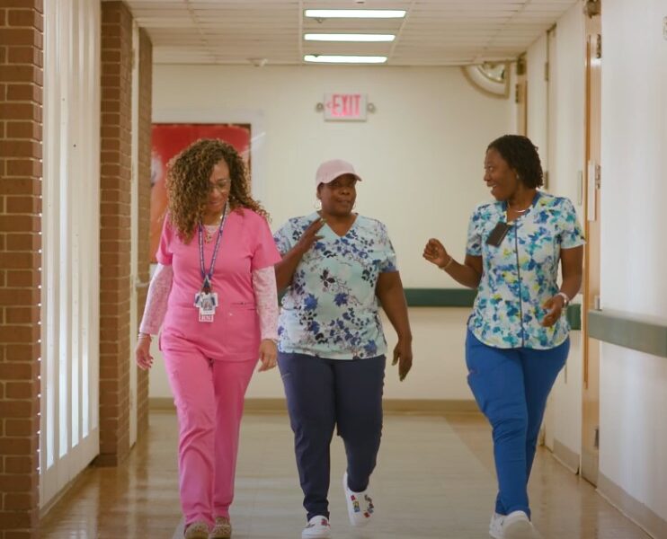 Three healthcare workers walking together in a hallway, smiling and talking to each other.