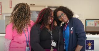 Three smiling diverse women in an office setting discussing professional development